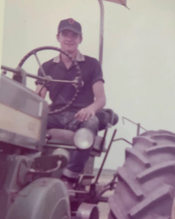 A young man in a cap at the steering wheel of a tractor, looking toward the camera.